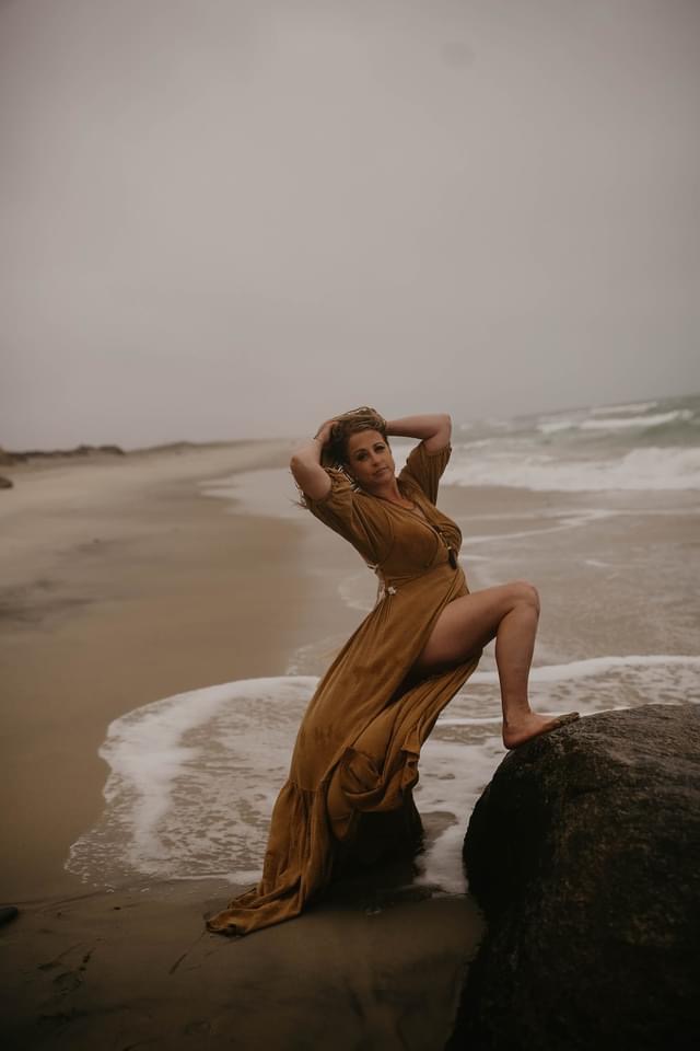 woman yellow dress leg up on a rock in the ocean